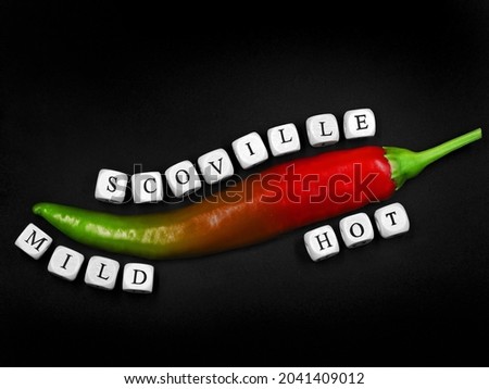 top view of a chilli with different degrees of ripeness on black background, from mild green to hot red, scoville described with white letter cubes
