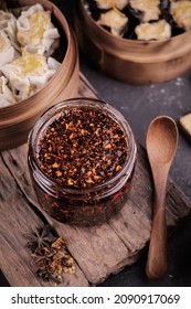 Top View Of Chilli Oil In Jar Served In Mason Jar With Wooden Chopping Board Under, Chili Oil Is A Condiment Made From Vegetable Oil  Infused With Chili Peppers, Commonly Served With Dumplings