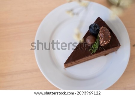 Top view of chocolate cake in white plat on wooden table decorating with chocolate ball, blueberry and choccolate with nut and rosmary on top. delicious and high calories food.