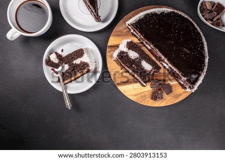 Top view of chocolate layer cake with berry filling, coffee and dessert plates on dark background. Cozy food composition with copy space.