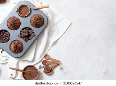 Top view of chocolate muffins flat lay in baking tray with slides of chocolate, chocolate chip, cocoa powder and chocolate sauce on white cutting board and white cloth with copy space - Powered by Shutterstock