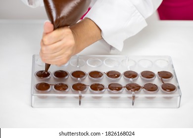 top view of chocolatier hands pouring melted dark chocolate into candy mold preparing luxurious handmade belgium confectionery. World Chocolate Day. Cooking video lessons. Culinary Blog concept