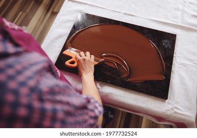 Top view of chocolatier holding cake scraber and cooling melted chocolate mass on a marble table. Closeup - Shutterstock ID 1977732524