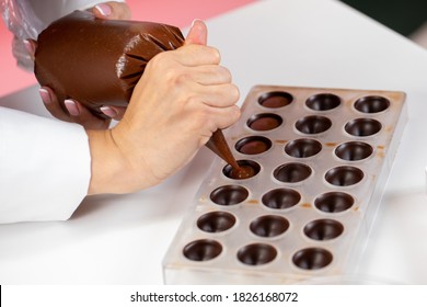 top view of chocolatier pouring caramel filling into chocolate mold preparing luxurious handmade Belgian candy. confectionary manufacturing small business idea concept. World Chocolate Day