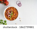 Top view of chole masala or chana local indian street food made of chickpeas, tomatoes and cumin decorated with red onion rings and parsley served on white wooden background. Image with copy space