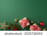 Top view of Christmas gifts with red bows, ornaments, and fir branches on a green backdrop setting