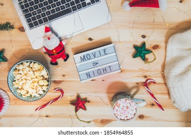 Top view Christmas Movie night concept. Flat lay composition with Movie night message on the board, laptop, popcorn bowl, decor, a cup of cocoa with marshmallows and warm plaid on wooden background