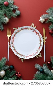 Top view Christmas table setting with empty plate, golden cutlery, decorative pine branches and ornaments.