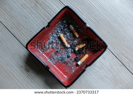 Top view of cigarette stubs in red ashtray. Warning, smoking addiction and health risk.