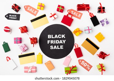 Top view of circle with black friday lettering near credit cards and toy shopping bags on white background
