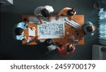 Top view of civil engineer team holding blueprint and standing at table with laptop, project plan and blueprint. Aerial view of skilled project manager planning and writing on sticky notes. Symposium.