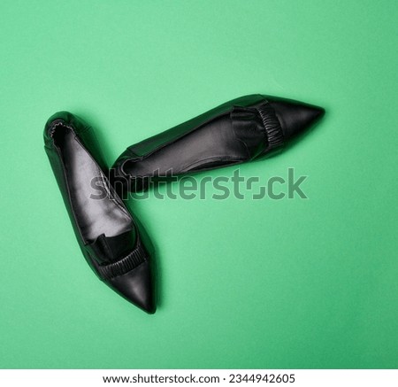 Top view of classy black pointed-toe leather shoes with wrinkled and ruffle details isolated on the soft green background. The concept of modern stylish footwear