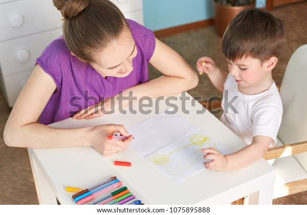 Top\
view of clever talented small boy draws car on paper with colourful\
mark pen, likes to make different pictures, spends time with his\
affectionate mother. Children and development\
concept