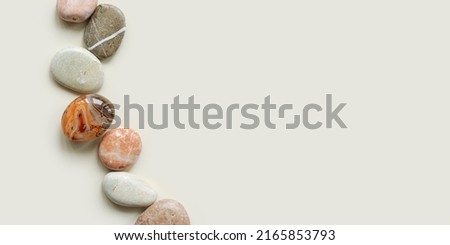Top view close up colored pebbles sea stones on sand color background. Row from natural round smooth stone neutral tones and sardonyx. Minimal style banner, summer concept, empty space for text.