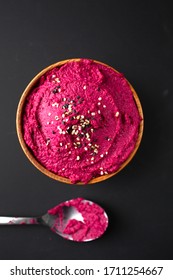 Top view and close up of a colorful beetroot hummus with spoon on a black background 