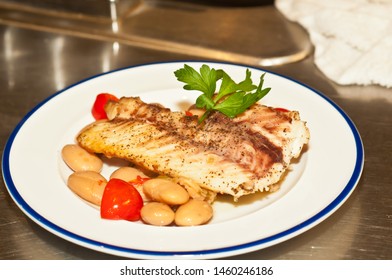 Top View, Close Distance Of A Freshly Prepared Filet Of Red Snapper Fish With A Base Of White Bean And Pepper Salad And Halved Cherry Tomatoes, On A Round, White Disth With A Blue Rim