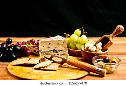 Top  view, close distance of spanish tapas of a wedge of blue cheese, cheese knife on a round, rare wood plate, bowls of olives, pistachio nuts with a variety of freshly picked grapes and crackers - Powered by Shutterstock