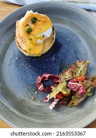 A Top View Close Up Food Shot Of Eggs Benedict, Eggs Royale With Fresh Vegetables, Salad On A Ceramic Blue Plate