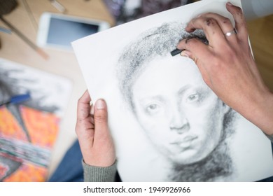 Top view of a close up of the hands of a person drawing a portrait in charcoal on a canvas. Concept of painting classes. Selective focus. Space for text.