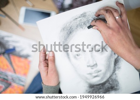 Top view of a close up of the hands of a person drawing a portrait in charcoal on a canvas. Concept of painting classes. Selective focus. Space for text.