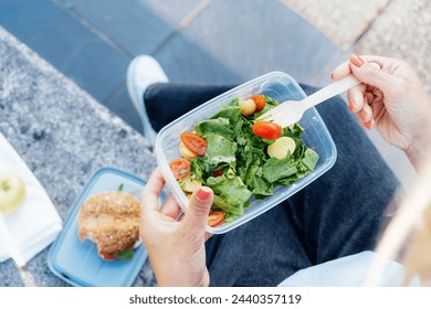 Top view close up lunch box with fresh salad and wooden folk in hand of woman sitting on the bench. Balanced diet lunchbox for weight loss. Healthy eating habits and well-being. Selective focus. - Powered by Shutterstock