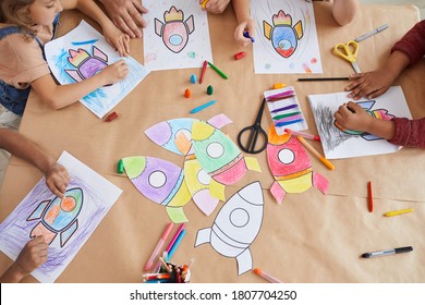 Top View Close Up At Multi-ethnic Group Of Kids Drawing Pictures Of Space Rockets With Crayons While Enjoying Art And Craft Class In Pre School Or Development Center, Copy Space