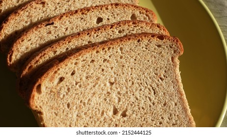 Top view close up of organic sliced bread isolated on green plate background. Bread slices food background. Sunlight shadows on surface of bread