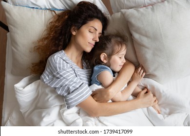 Top view close up peaceful loving mother and little daughter sleeping on soft pillow together, relaxing lying in cozy bed under warm blanket, caring young mum hugging sleepy preschool girl - Powered by Shutterstock