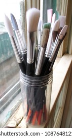 Top view close up of a selection of paint brushes in a glass jar inside a pottery studio

