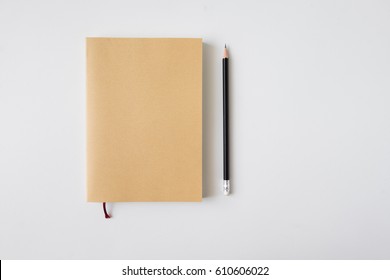 Top View Of Closed Blank Craft Paper Cover Notebook With Pencil On White Desk Background