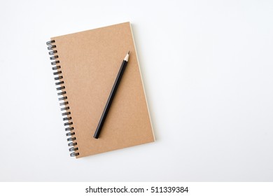 Top view of closed spiral blank recycled paper cover notebook with pencil on white desk background