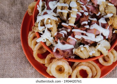 A Top View Closeup Of French Fries, Ham, Onion Rings With White Sauce On Top On An Orange Spiral Plate