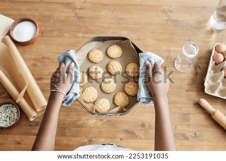 Top view closeup of little girl holding tray with homemade cookies while enjoying baking in kitchen against wooden background