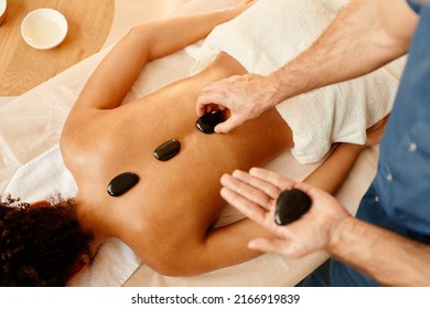 Top View Closeup Of Male Therapist Laying Stones On Back Of Young Woman In Relaxing SPA Session, Copy Space