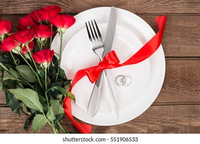 Top View Closeup Of Romantic Dinner Serving With A Bouquet  Red Roses And Ring Above The White Plate