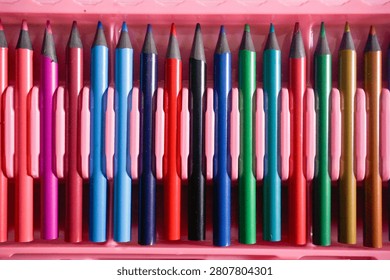 Top view close-up of a row of various colorful pencils arranged neatly inside a pink plastic stationary case or tray.