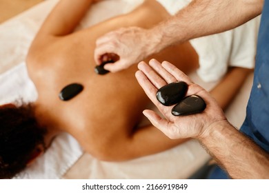 Top View Closeup Of Young Man Laying Stones On Back Of Young Woman In Relaxing SPA Session, Copy Space