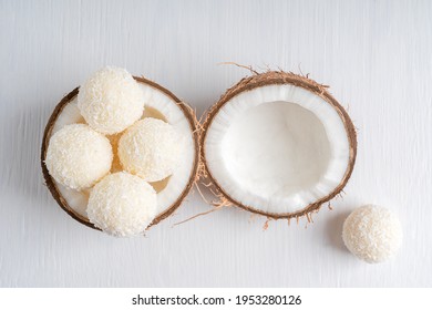 Top view of coconut truffles or homemade vegetarian energy balls with a filling of sweetened shredded coconut and curd cheese served in halved fresh coconut on white wooden table. Horizontal image