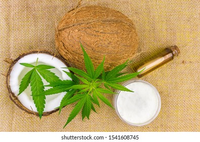 Top View Of Coconuts, Cannabis Leaves, CBD Oil And Lotion On Hemp Cloth