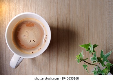 Top View Of Coffee Cup Mixed Milk Froth Or Creamer And Ivy Plant On Wooden Table With Copy Space, Background Image Of Drinks On Wood Texture In Morning Sunlight Minimalist Style And Convey Relaxation.