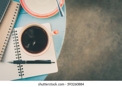 Top View Of Coffee Cup With Notebooks And Pen On Blue Round Wood Table With Vintage Filter Effect