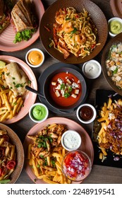 Top view of colorful food on wooden table in restaurant cafe. Pasta with shrimps. Caesar salad with chicken. Sandwiches. Various sauces. Tomato soup. French fries, omelette, grilled meat. Vertical. - Shutterstock ID 2248919541
