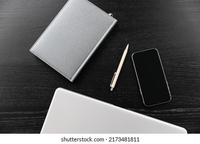 Top view of the composition against a background of ebony. Closed diary with gray leather cover, gold pen, closed silver notepad, phone. Desk in the office.  Free space for text. Space for copying.