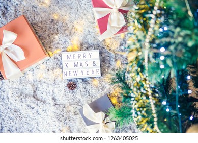 Top view composition of lighted box with Merry Christmas and New year wishes and presents in colorful festive wrapping tied with bow under xsmas tree branches. Gift Background, copy space