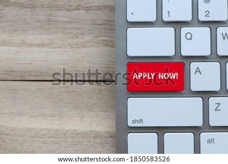 Top view of computer keyboard with a red key written with Apply Now! on wooden background with copy space.