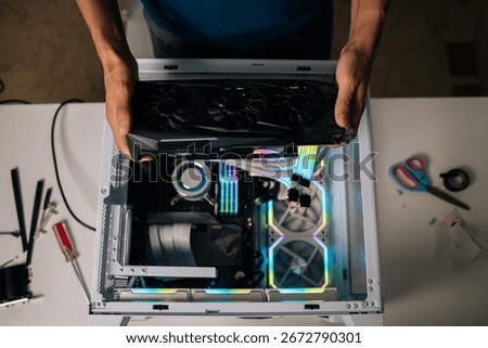 Top view of computer technician installing high-end graphic card into custom gaming pc, showcasing vibrant rgb lighting and advanced water cooling for peak performance enhancement.