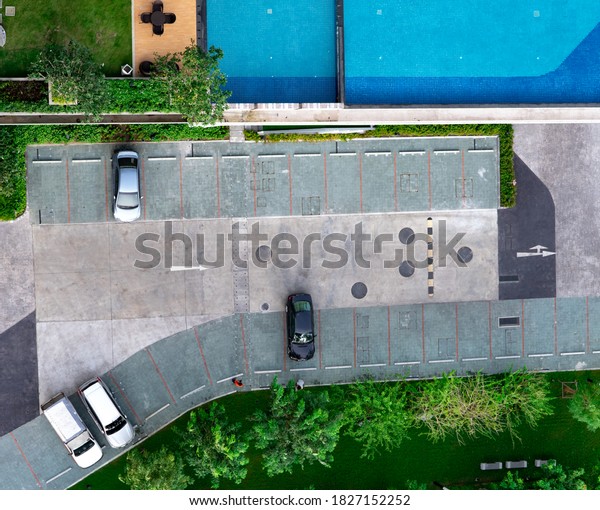 Top view concrete car parking lot, swimming pool,\
and garden of apartment. Aerial view of car parked at car parking\
area of condo. Outdoor parking space with empty slot. One way\
traffic sign on road.