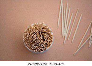 A top view of a container filled with wooden toothpicks, with a few toothpicks scattered nearby on a pastel background, dental hygiene concept  - Powered by Shutterstock