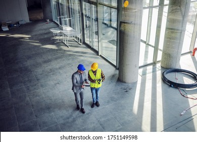 Top view of contractor and architect walking around building in construction process and talking about how they gonna build it.
