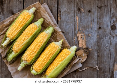 top view of cooked and uncooked corn cobs on left side and wooden background with copy space